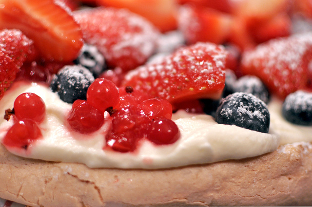 A closeup of a pavlova with berries and cream on top.